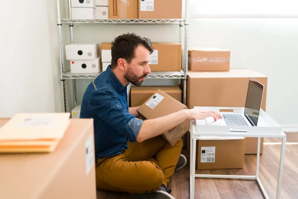 Dono de e-commerce mexendo no computador cercado de embalagens de papelão